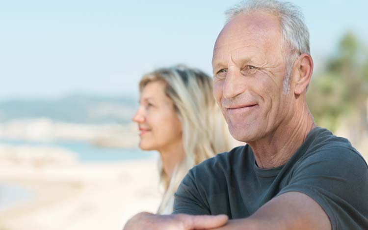Mann mittleren Alters am Strand mit Partnerin aufs Meer blickend